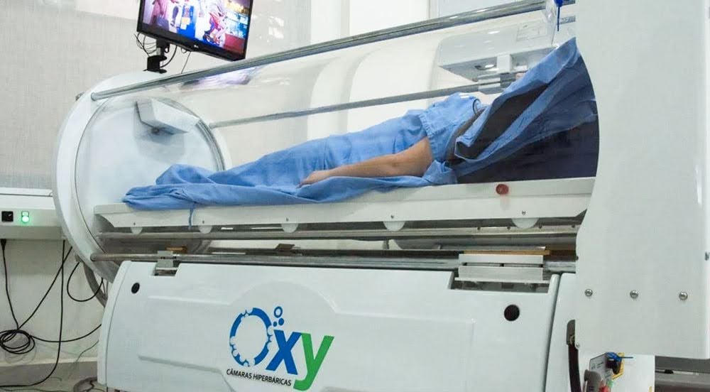 Casa hiperbárica: câmara de oxigenoterapia com um paciente dentro assistindo à TV durante sua sessão.